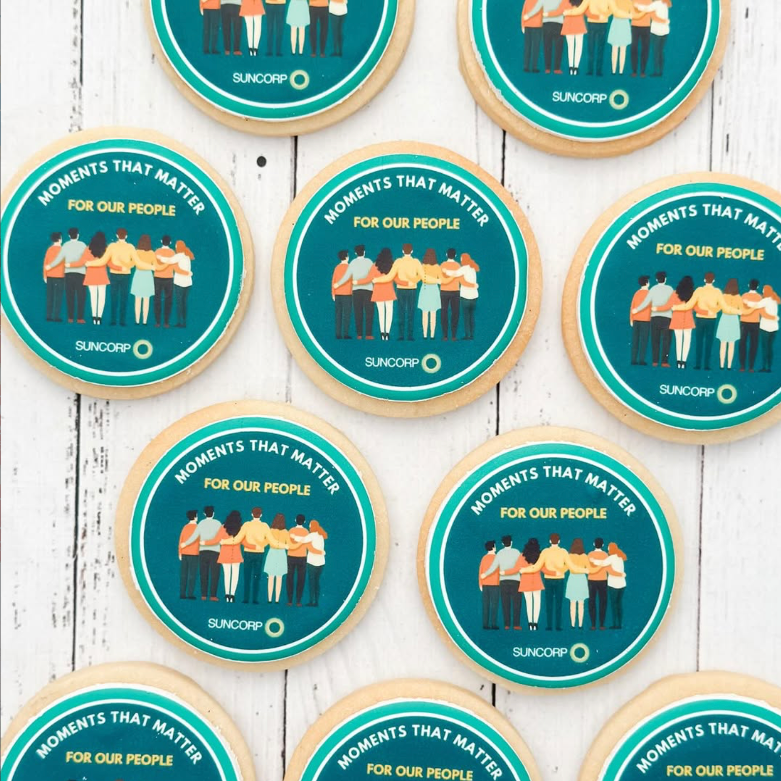 Suncorp branded cookies with illustrations of people and text on a wooden surface