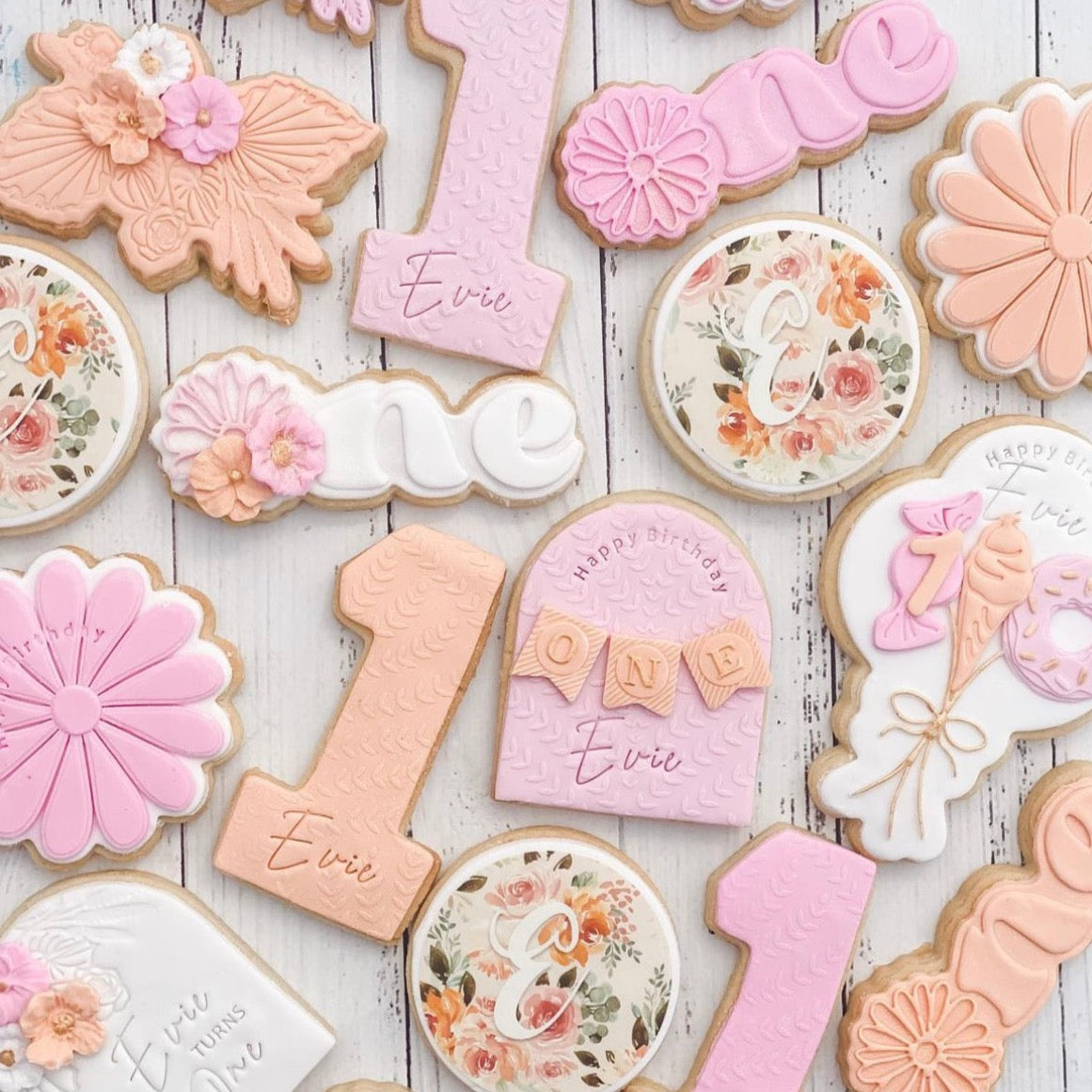 A variety of decorated cookies with numbers, floral patterns, and personalized edible images on a wooden surface.