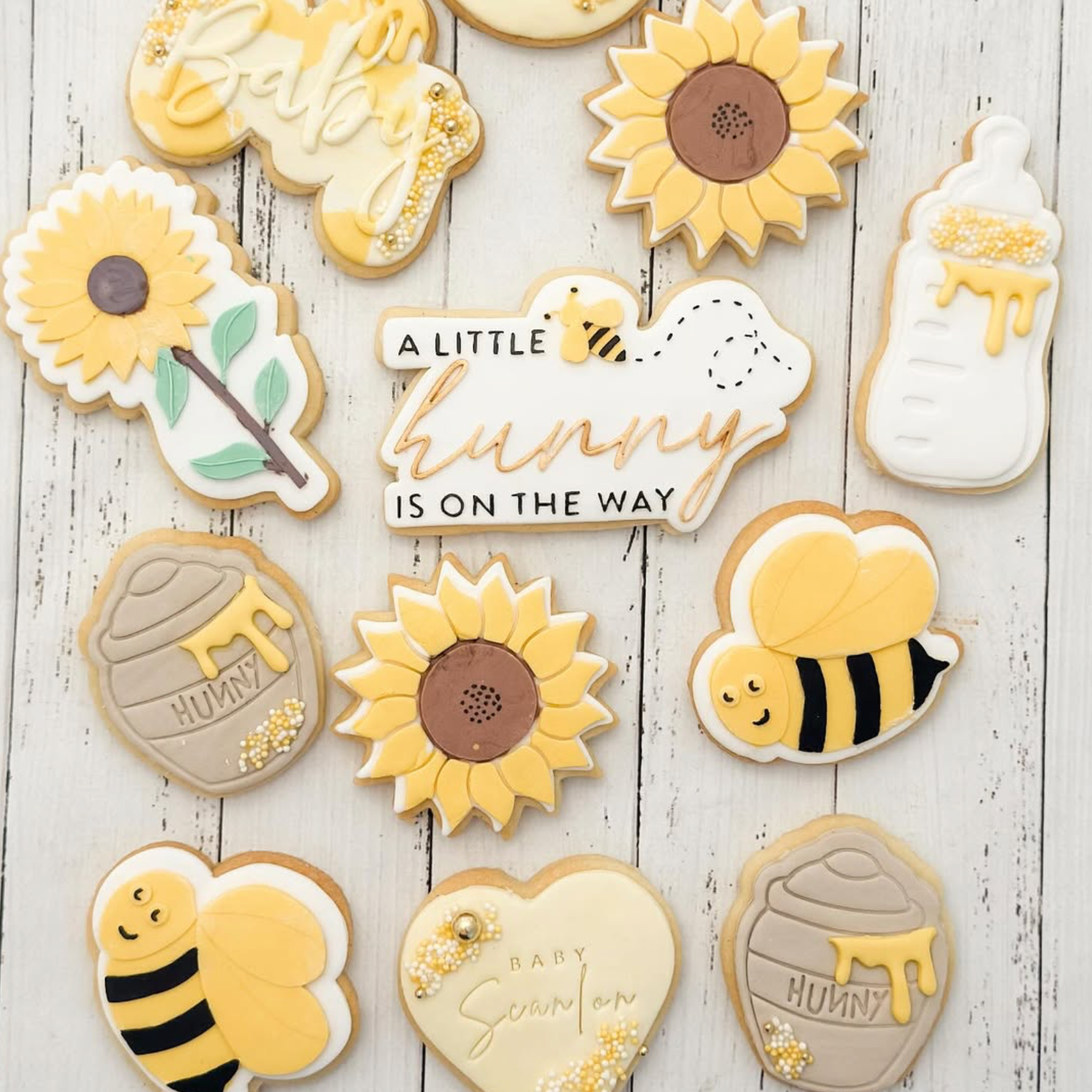 Decorative cookies with bee, sunflower, and 'A Little Hunny is on the Way' text on a wooden surface.