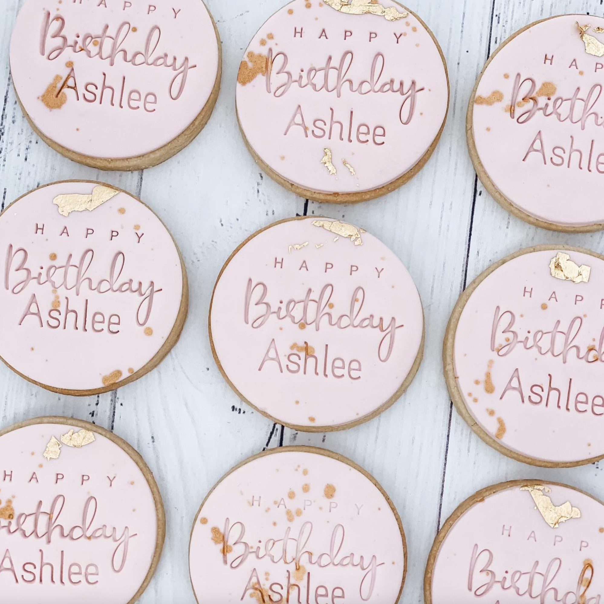 A collection of round cookies with a fondant topping, personalized with the name 'Ashlee' and the phrase 'Happy Birthday'. The cookies are decorated with a marble pattern and gold accents.