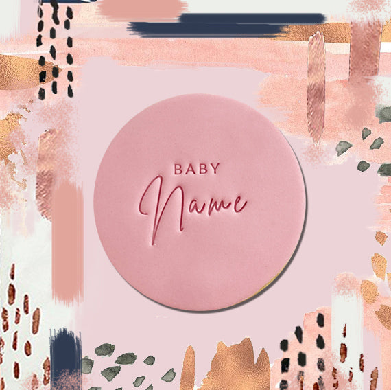 A round pink cookie with the words 'BABY Name' written in a cursive script, presented on a card with abstract patterns in the background.